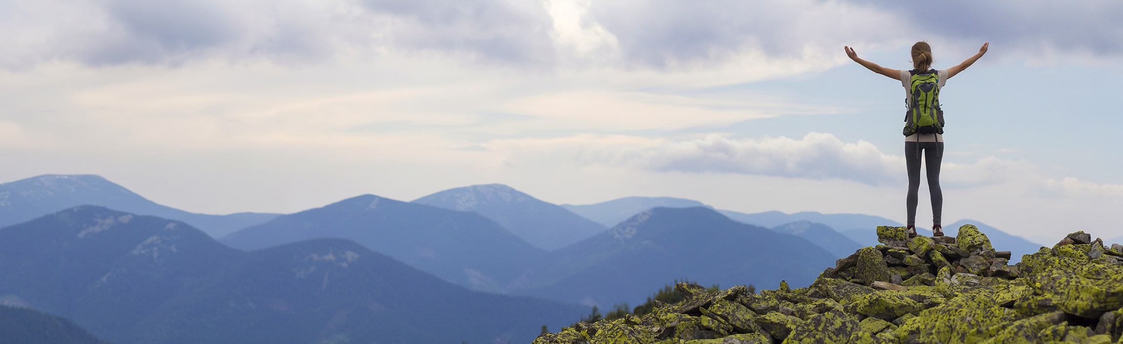 woman standing on top a mountain looking at other mountains